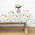 Floral patterned tablecloth on a wooden table with a vase of flowers and glasses.